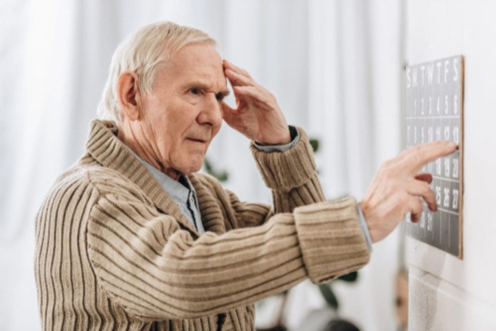 Senior man struggling with memory while pointing at a calendar on the wall